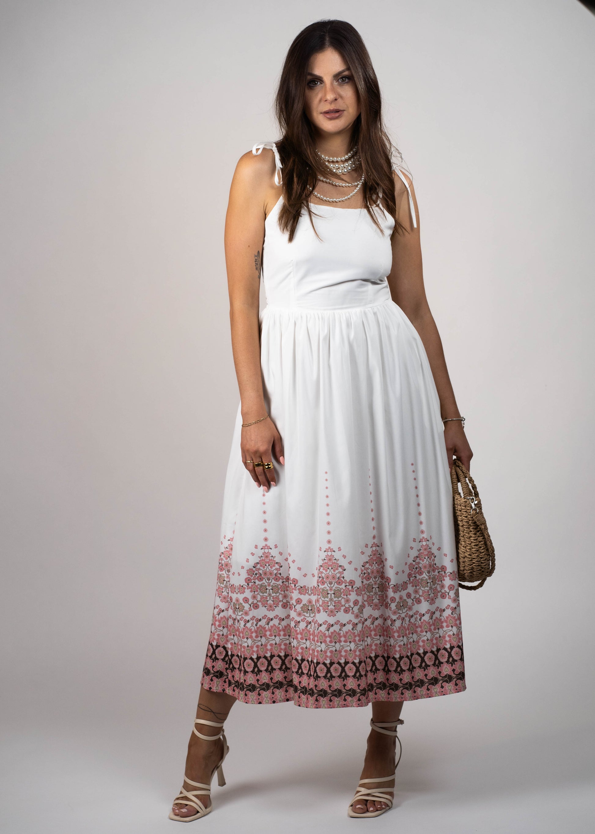 White maxi midi dress with pockets and pink flowers at the hem and ties on the shoulders. Elegant and feminine, perfect for a stylish summer look