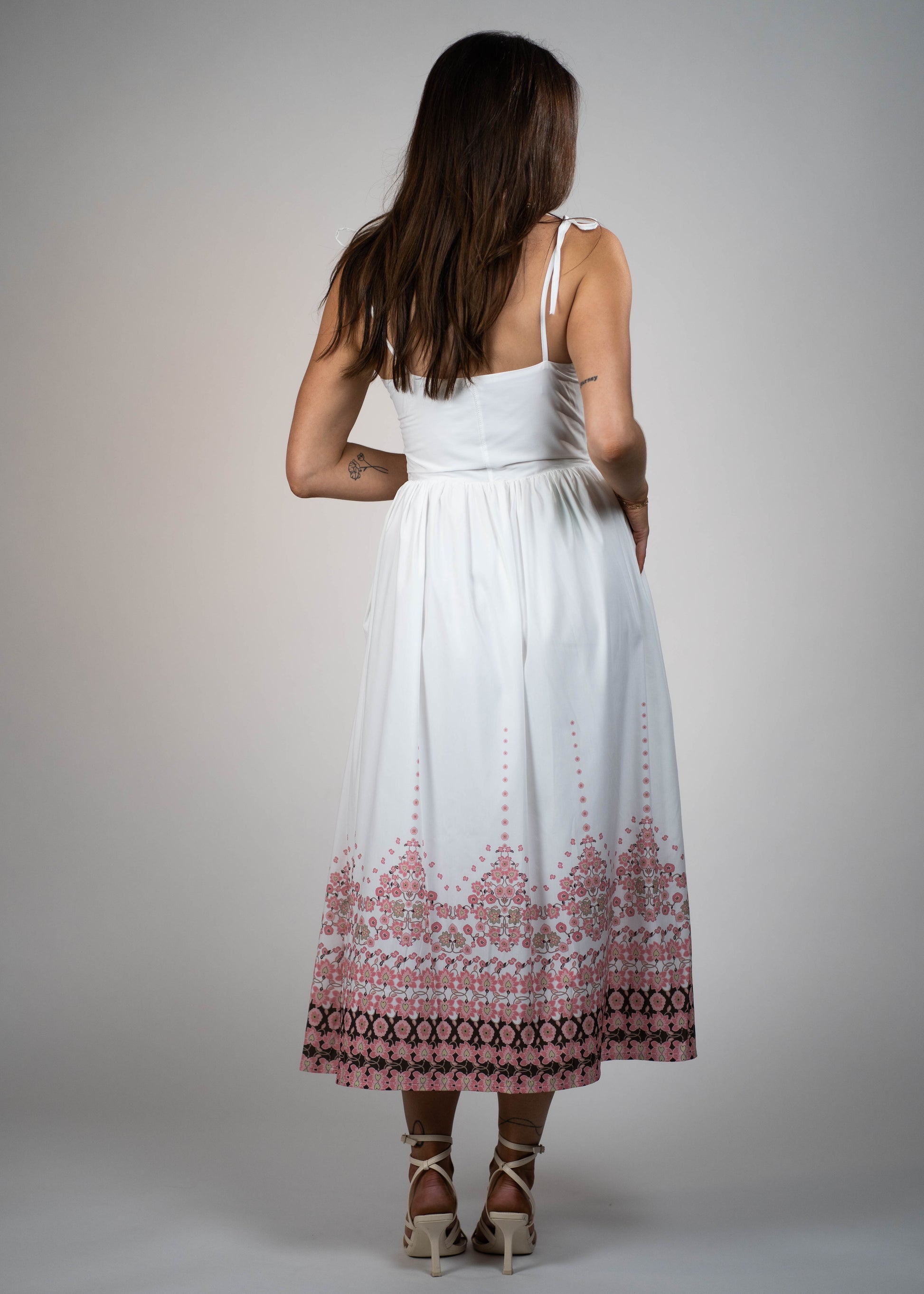 White maxi midi dress with pink flowers at the hem and ties on the shoulders. Elegant and feminine, perfect for a stylish summer look