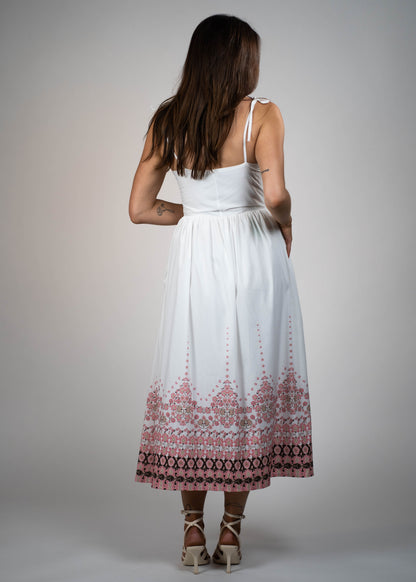 White maxi midi dress with pink flowers at the hem and ties on the shoulders. Elegant and feminine, perfect for a stylish summer look