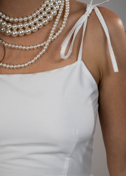 White maxi midi dress with pockets and pink flowers at the hem and ties on the shoulders. Elegant and feminine, perfect for a stylish summer look