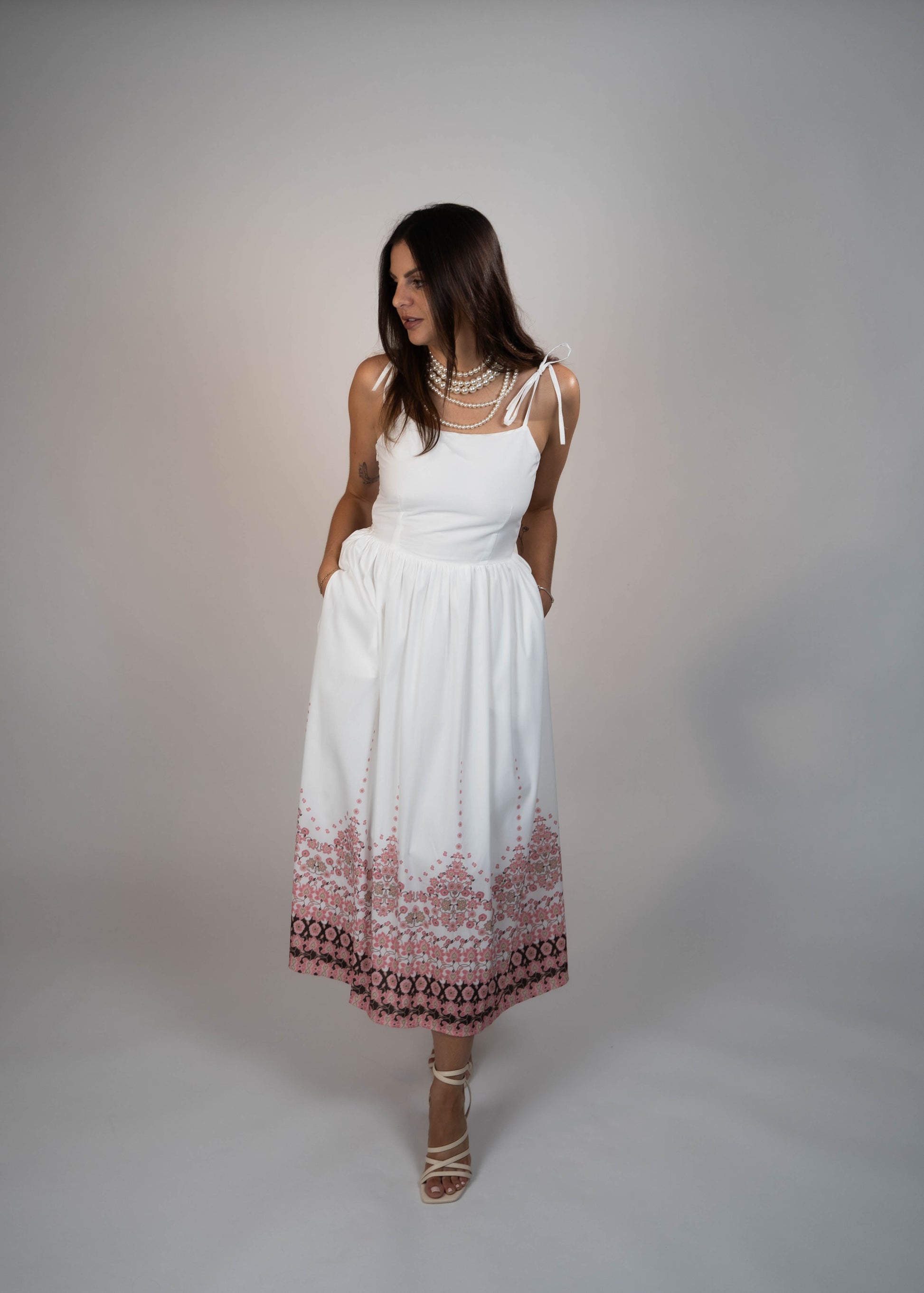 White maxi midi dress with pockets and pink flowers at the hem and ties on the shoulders. Elegant and feminine, perfect for a stylish summer look